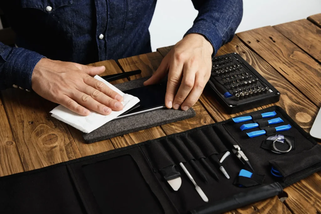 master-cleans-mobile-phone-after-successful-restoration-with-white-cloth-near-his-professional-instruments-tool-bag-wooden-table-1-scaled